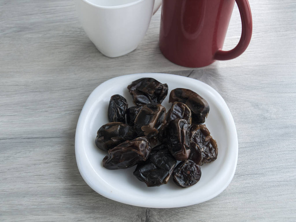 Alimentation saine : dattes séchées sur une soucoupe, tasse rouge, tasse blanche sur une table grise en bois. Vue de dessus. Espace de copie
 - Photo, image