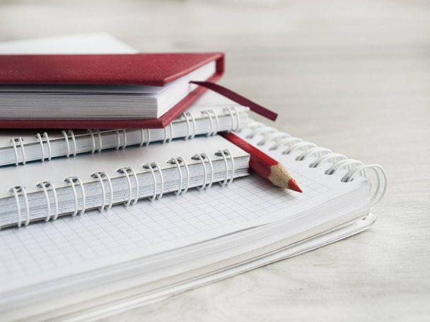 Office accessories: a red notepad, a white notepad and red pencil on a wooden gray desk. Back to school. ?lose-up. Top view. Copy space - 写真・画像