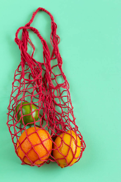 ストリングバッグにマルチカラーの柑橘類を持つ概念的な明るいカラフルな背景。テキスト用のスペース. - 写真・画像