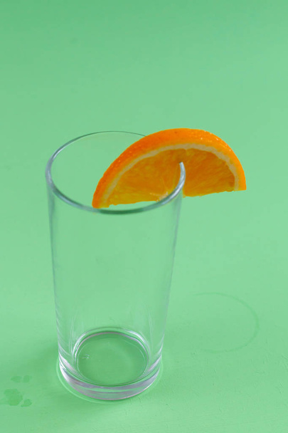 Порожнє скло з апельсиновою скибочкою ізольовано на зеленому фоні
 - Фото, зображення