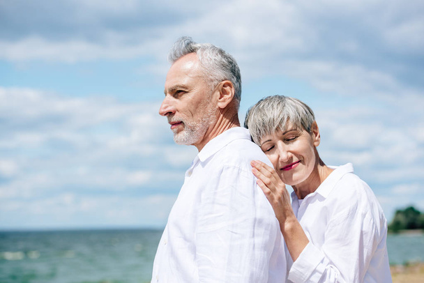 happy senior couple in white shirts standing under blue sky in sunny day - Foto, Imagem