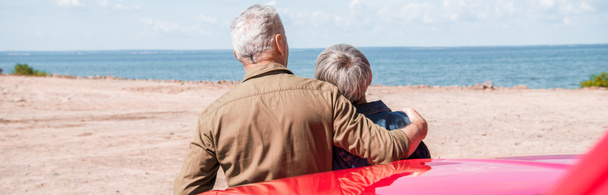 панорамный вид на пожилую пару туристов, стоящих рядом с автомобилем и обнимающихся на пляже
 - Фото, изображение