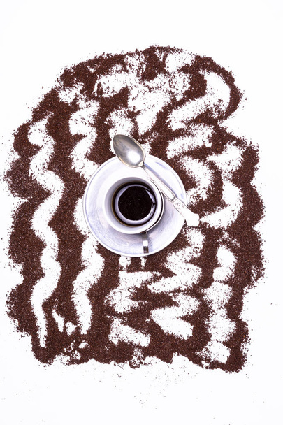 散らばったコーヒーの穀物のパターンによって形成されたスタイリッシュな背景にスプーンとコーヒーと金属皿の小さなカップ。カップを強調するクリエイティブなグラフィック背景を持つトップダウンビュー. - 写真・画像