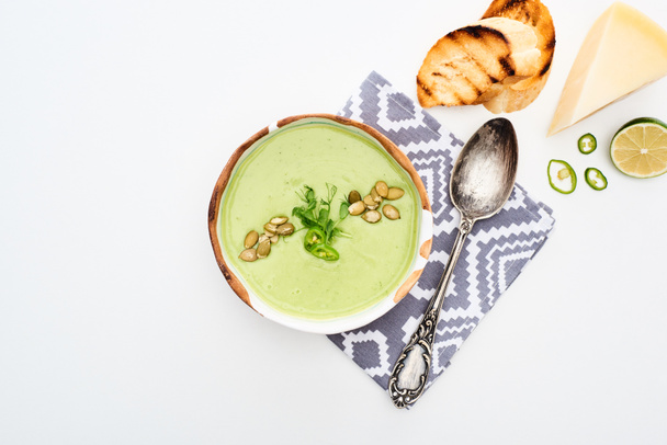 vista superior de la deliciosa sopa de verduras verde cremosa servida en la servilleta cerca de la cuchara con croutons a la parrilla y queso aislado en blanco
 - Foto, Imagen