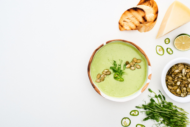 vista superior de deliciosa sopa de legumes verde cremoso com brotos, croutons grelhados e sementes de abóbora isoladas em branco
 - Foto, Imagem
