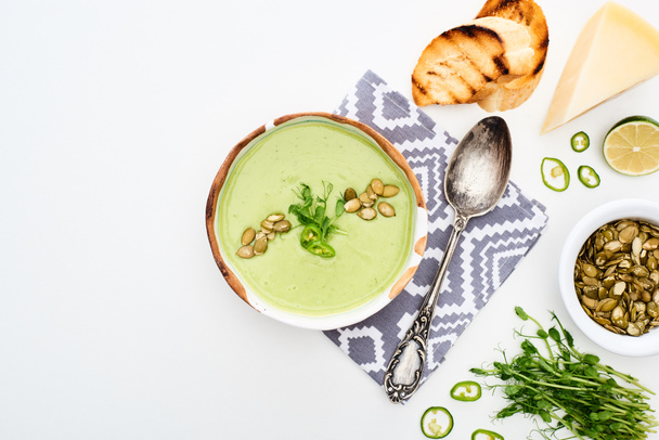 pohled na lahodnou smetanovou zelenou zeleninovou polévku s kapustou, grilované croutony a dýňová semena podávané na ubrousku na bílém - Fotografie, Obrázek