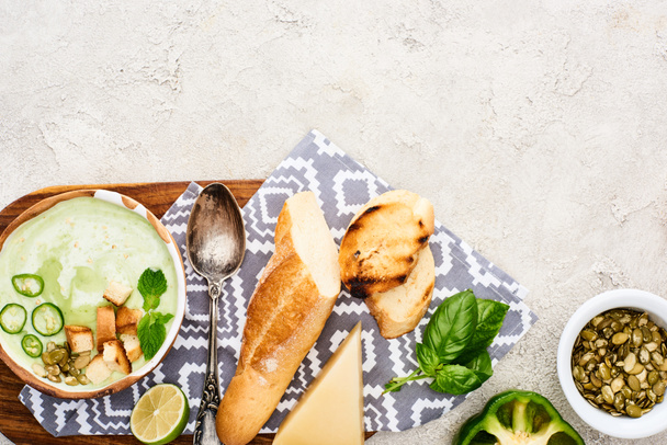 вид на зеленый овощной сливочный суп на деревянной доске с салфеткой и ингредиентами возле семян тыквы
 - Фото, изображение