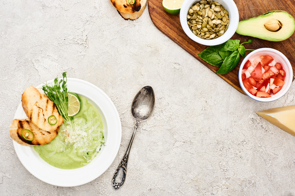 вид на зеленый сливочный суп возле деревянной доски со свежими ингредиентами
 - Фото, изображение