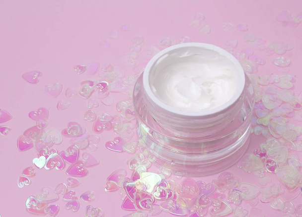 Cosmetische crème lotion jar op roze holografische hart confetti sparkles achtergrond met Kopieer ruimte. - Foto, afbeelding