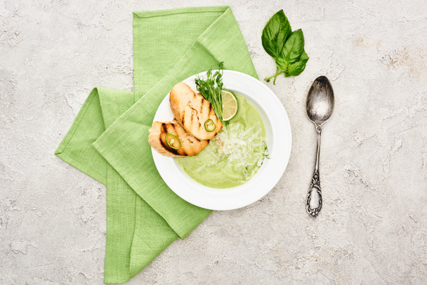top view of delicious creamy green vegetable soup with croutons served with napkin and spoon - 写真・画像