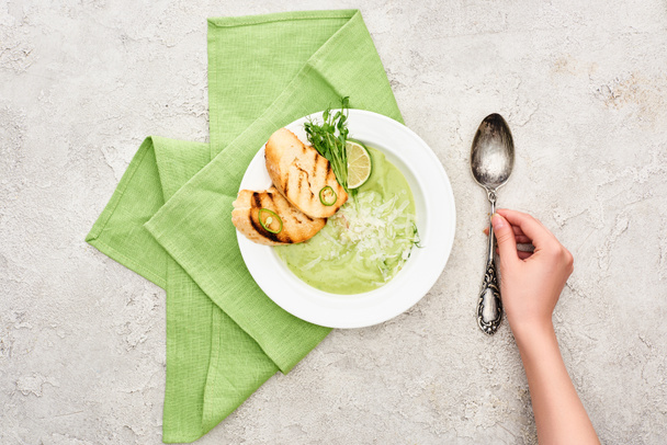 vista parcial de la mujer poniendo cuchara cerca de deliciosa sopa de verduras verde cremosa servida con croutons
 - Foto, Imagen