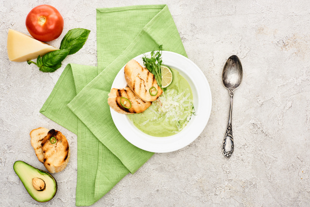 vista superior de la deliciosa sopa verde cremosa con croutons cerca de ingredientes frescos
  - Foto, imagen