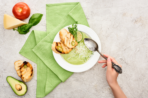 vista recortada de la mujer sosteniendo cuchara cerca del plato con deliciosa sopa de verduras verde cremosa con croutons
 - Foto, Imagen