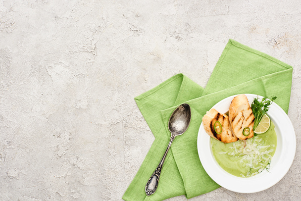 vista superior de deliciosa sopa de legumes verde cremoso com brotos e croutons servidos com guardanapo e colher
 - Foto, Imagem