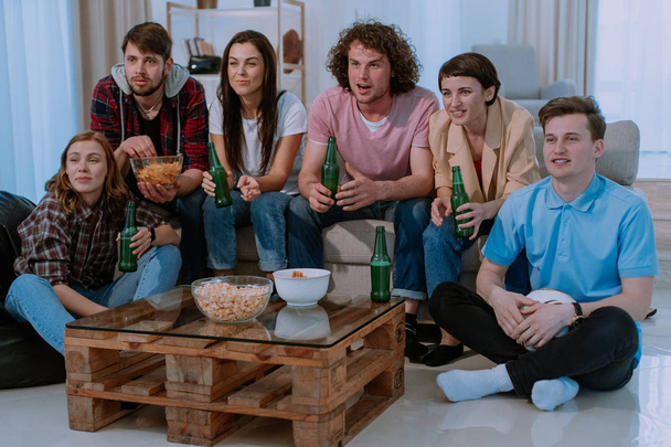 Потерять группу из нескольких этнических друзей смотреть сосредоточены и взволнован футбольный матч перед телевизором в гостиной они пьют пиво и едят закуски
 - Фото, изображение