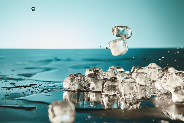 transparent melting ice cubes with puddles on emerald and white background - Φωτογραφία, εικόνα