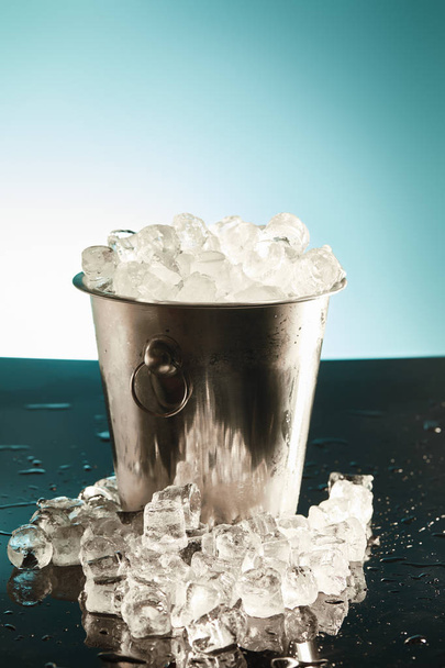 cubos de gelo transparentes em balde de metal com gotas de água na superfície sobre fundo esmeralda e branco
 - Foto, Imagem