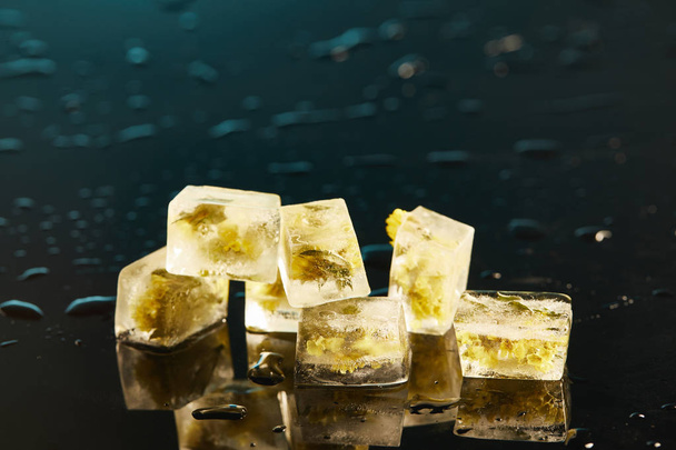 стопка прозрачных кубиков льда с замороженными цветами на изумрудном фоне
 - Фото, изображение
