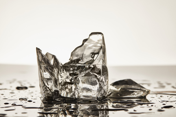 cubos de gelo de fusão transparentes com poças no fundo branco
 - Foto, Imagem