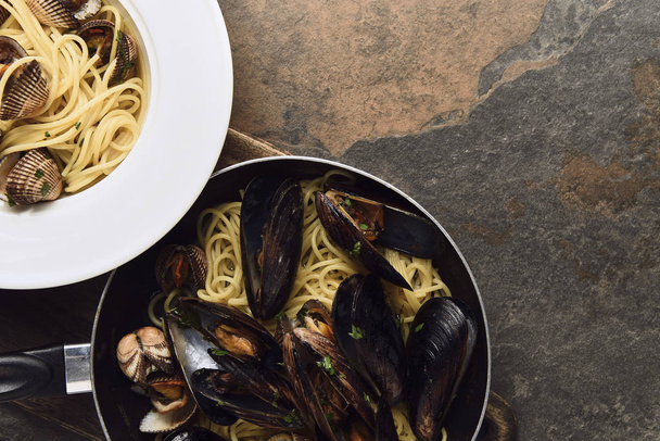 top view of delicious pasta with mollusks and mussels on wooden cutting board on weathered grey background - 写真・画像