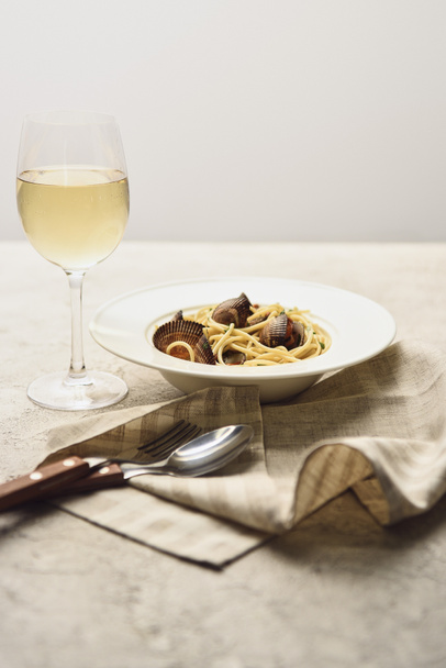 smakelijke Italiaanse pasta met zeevruchten geserveerd met witte wijn, servet en bestek geïsoleerd op grijs - Foto, afbeelding
