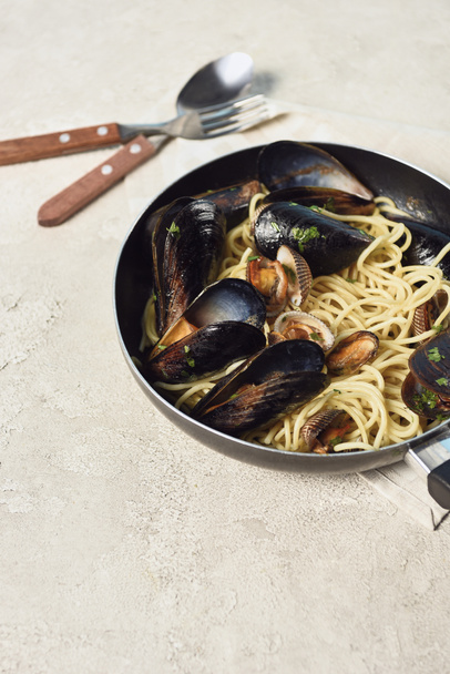 delicious pasta with seafood in frying pan near cutlery on textured grey background - Photo, Image