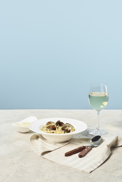 köstliche italienische Spaghetti mit Meeresfrüchten serviert mit Weißwein auf Serviette in der Nähe von Besteck isoliert auf blau - Foto, Bild