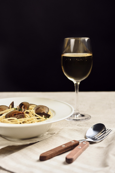 вкусные итальянские спагетти с морепродуктами подается с белым вином на салфетке возле столовых приборов, изолированных на черном
 - Фото, изображение