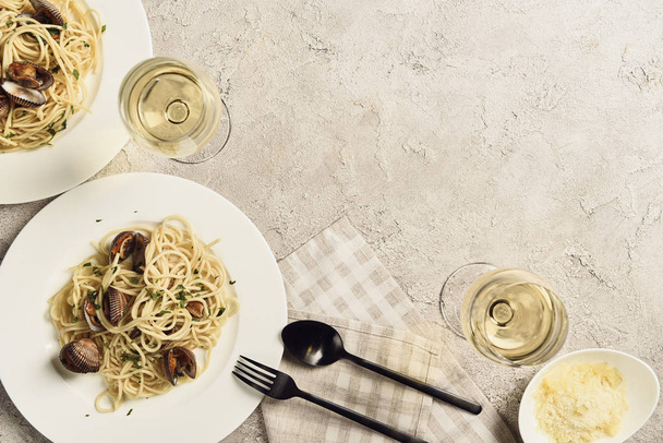 Top uitzicht van heerlijke pasta met zeevruchten geserveerd met witte wijn en geraspte kaas op getextureerde grijs oppervlak met Kopieer ruimte - Foto, afbeelding