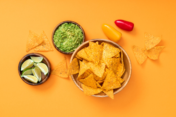 top view of crispy Mexican nachos, guacamole, limes and bell peppers on orange background - Fotografie, Obrázek