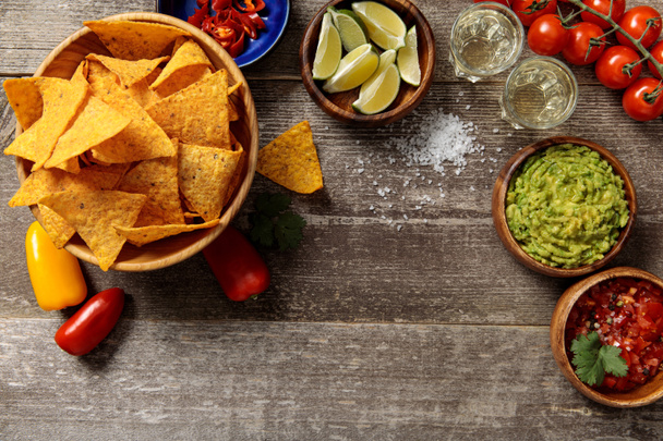 Blick auf mexikanische Nachos mit Tequila, Guacamole und Salsa auf verwittertem Holztisch - Foto, Bild