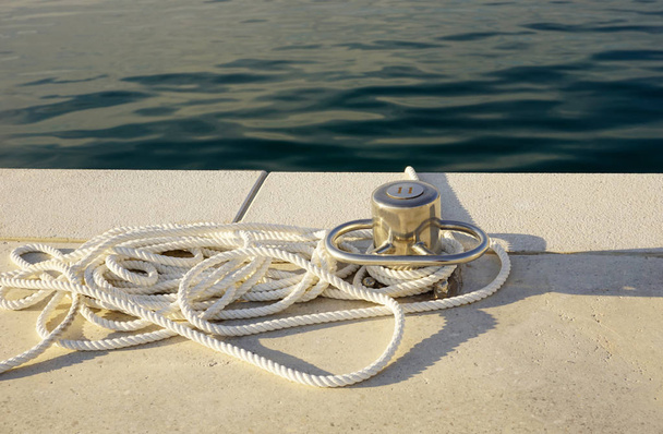 Деталь з яхти морський, біла мотузка і швартовий стовп біля блакитного моря
 - Фото, зображення