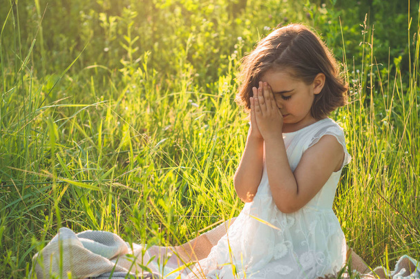 小さな女の子は、美しい夕日の間に野原で祈って、彼女の目を閉じました。信仰のための祈りの概念で折り畳まれた手 - 写真・画像