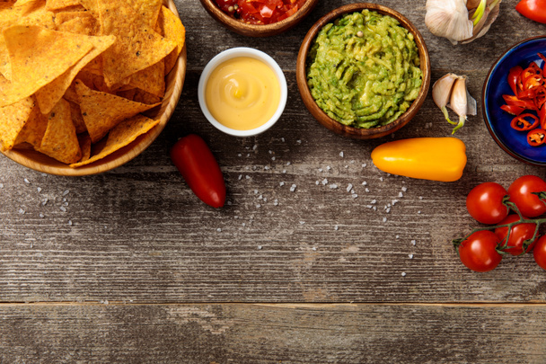 top view of Mexican nachos served with guacamole, cheese sauce and salsa on wooden table with salt - Photo, Image