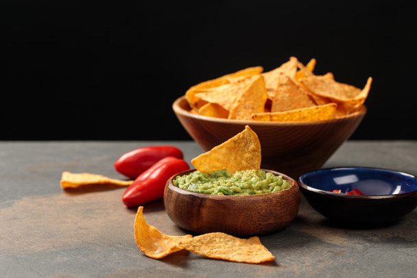 traditional Mexican nachos with guacamole and chili peppers on stone table isolated on black - 写真・画像