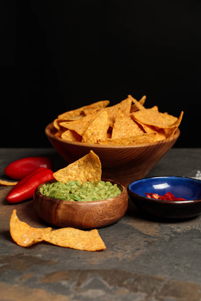 tasty Mexican nachos with guacamole and chili peppers on stone table isolated on black - Foto, Imagen