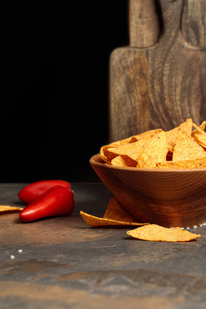 Mexican nachos with salt and chili peppers near wooden cutting boards on stone table isolated on black - Foto, Bild