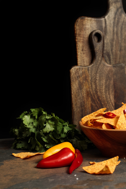 Mexican nachos with salt and chili peppers near wooden cutting boards and parsley on stone table isolated on black - Foto, Imagen