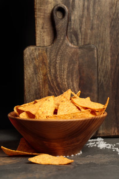 Mexicaanse nacho's met zout in de buurt van houten snijplanken op stenen tafel geïsoleerd op zwart - Foto, afbeelding