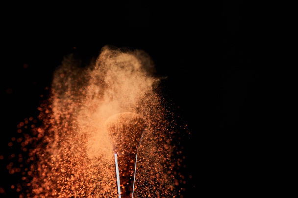 escova cosmética com explosão de pó de laranja no fundo preto
 - Foto, Imagem