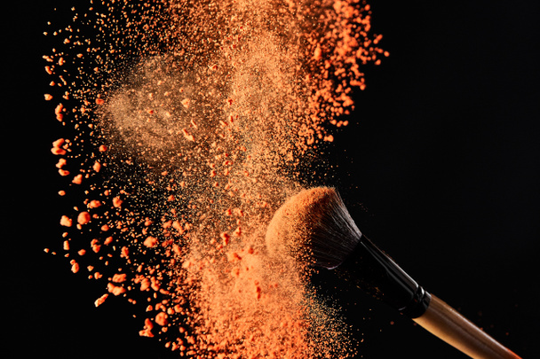 καλλυντικό πινέλο με πολύχρωμη έκρηξη πορτοκαλί σκόνης σε μαύρο φόντο - Φωτογραφία, εικόνα