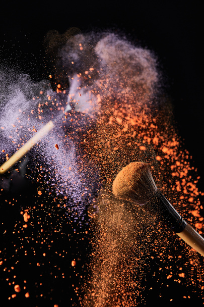 siyah arka plan üzerinde renkli turuncu ve mor toz patlama ile kozmetik fırçalar - Fotoğraf, Görsel