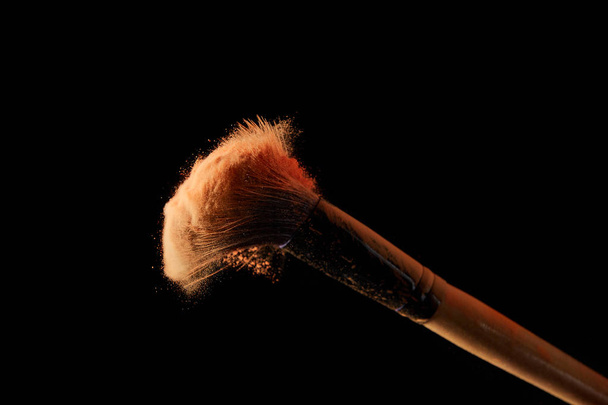 косметическая кисть с красочным оранжевым порошком на черном фоне
 - Фото, изображение