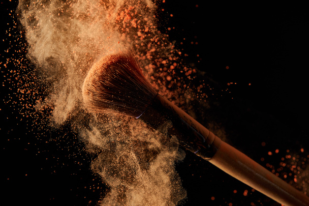soft cosmetic brush with colorful orange powder explosion on black background - Foto, Imagen