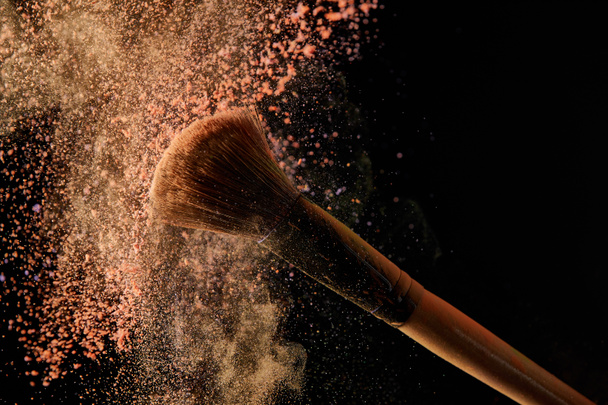 soft cosmetic brush with colorful orange powder explosion on black background - Foto, Imagem