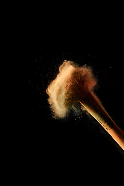 cosmetic brush with colorful orange powder explosion on black background with copy space - Foto, Imagem