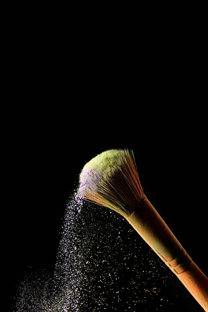cosmetische borstel met kleurrijke verstrooide geel en Violet poeder op zwarte achtergrond - Foto, afbeelding