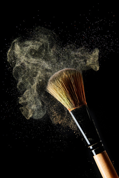 cepillo cosmético con polvo amarillo claro sobre fondo negro
 - Foto, Imagen
