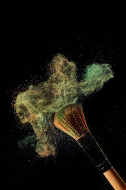 brosse cosmétique avec explosion de poudre verte et orange sur fond noir
 - Photo, image