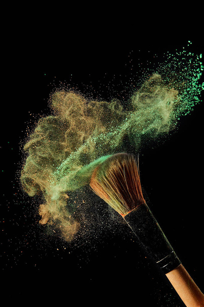 cosmetic brush with green and orange powder on black background - Photo, Image
